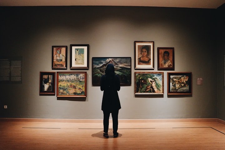 Visitor in front of framed paintings in a gallery